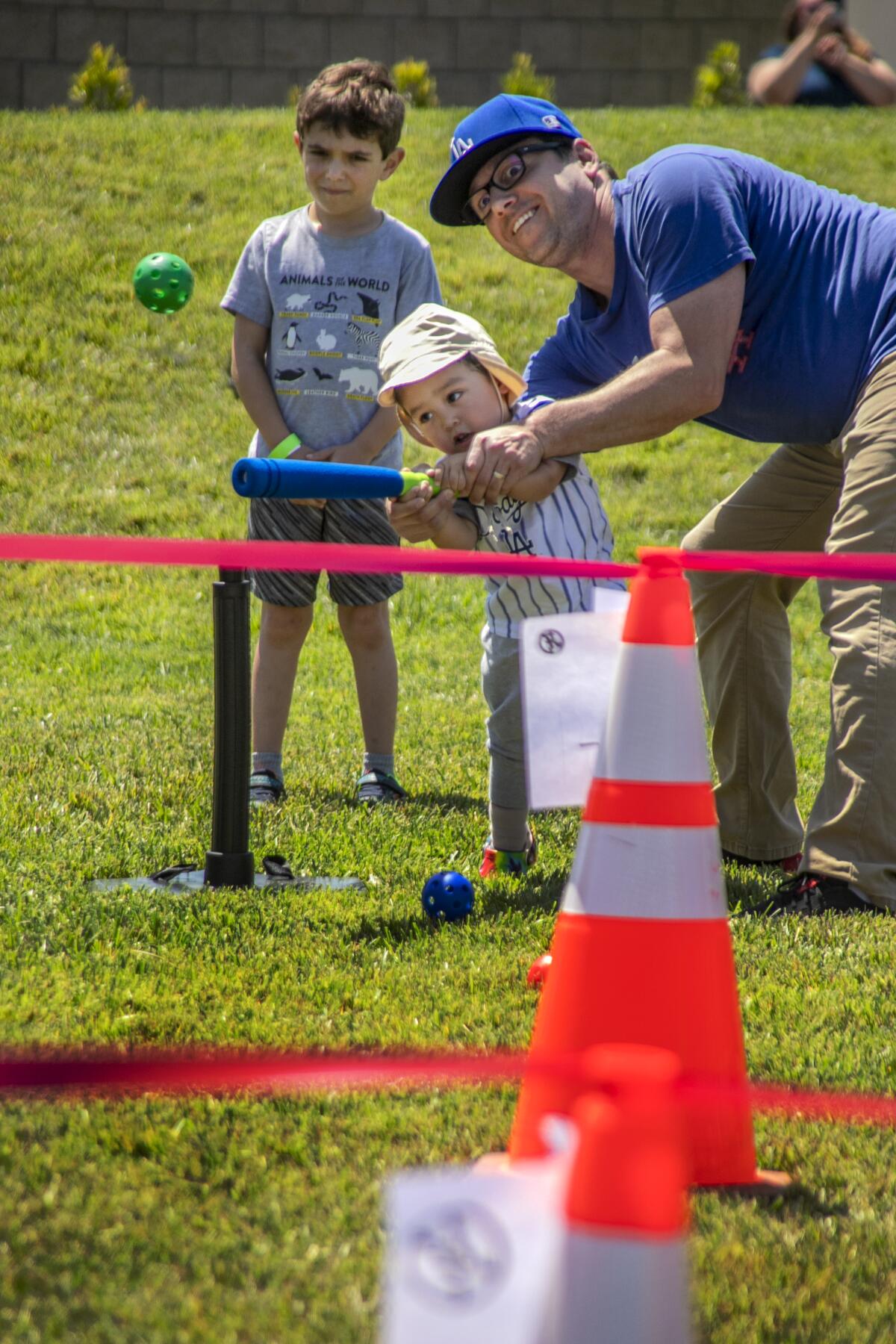 With dad Matthew helping and Jacob Hurwitz, 7, looking on, 2-year-old Martin Langer smacks a wiffle ball.
