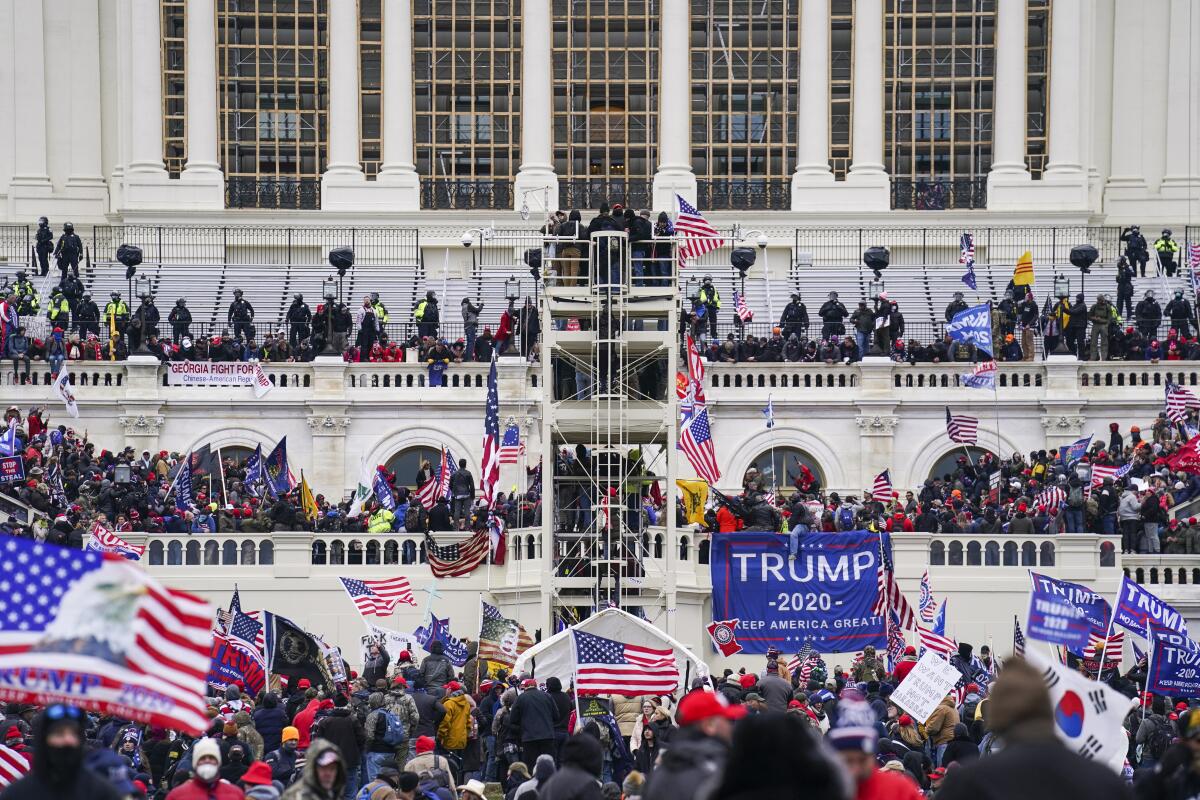 Crowds, some holding U.S. flags and Trump signs swarm a white building with columns