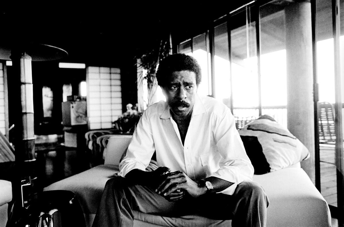 A black-and-white shot of Richard Pryor sitting on the edge of a bed