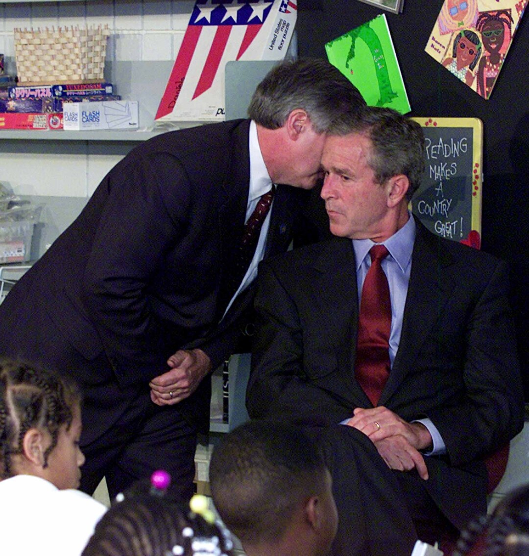 An aide whispers in President Bush's ear as he sits in a classroom