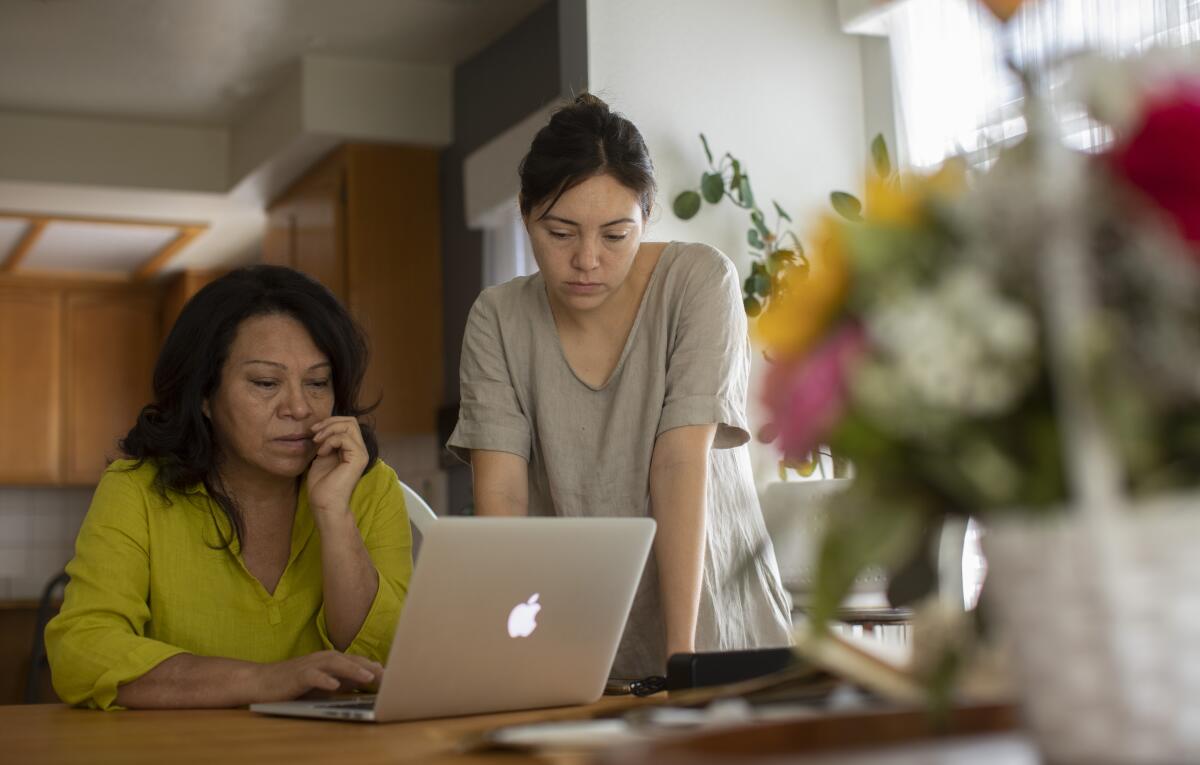 A woman sits at a laptop with another woman standing next to her