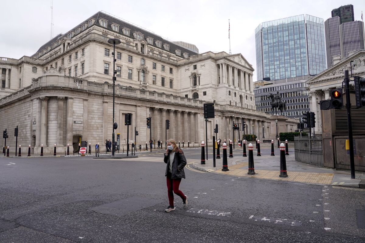 A woman wears a face mask while walking crossing a road outside the Bank of England, in the financial district, known as The City, in London, Monday, Dec. 13, 2021. While many people will re-start working from home, the British government raised the country's official coronavirus threat level on Sunday, warning the rapid spread of omicron "adds additional and rapidly increasing risk to the public and health care services" at a time when COVID-19 is already widespread. (AP Photo/Alberto Pezzali)