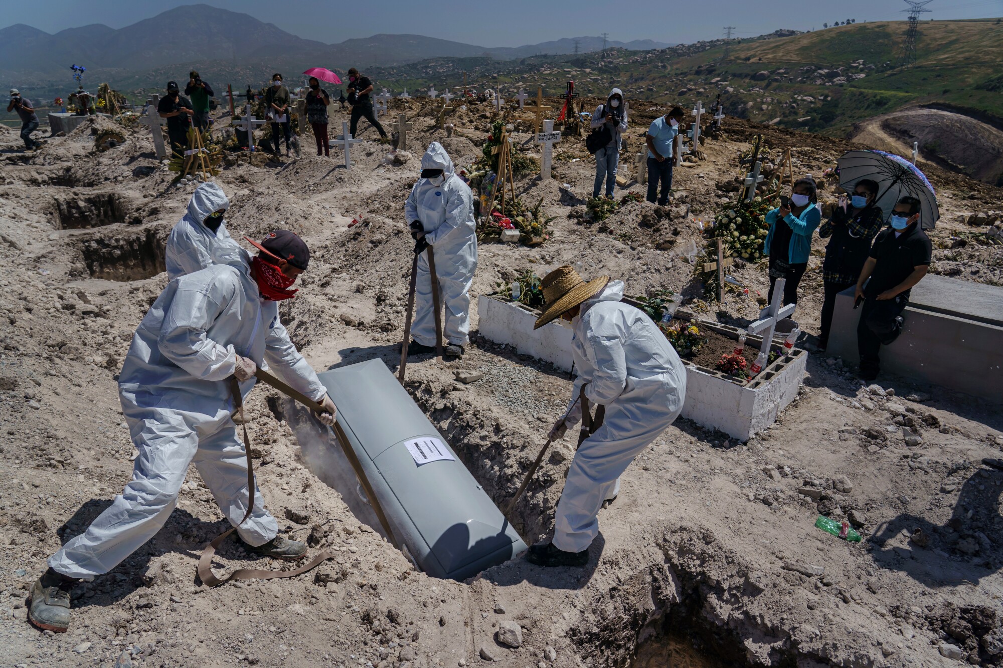 Cemetery workers lower the casket of Juan Velasco, who died of COVID-19 symptoms, as his family, to the right, watches the burial at Tijuana's Municipal Cemetery No. 13.