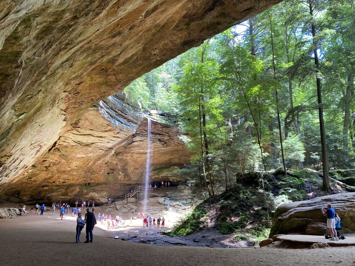 Visitors explore Ash Cave, a massive recess cave in Hocking Hills State Park, in Ohio. A waterfall drops from the rim.
