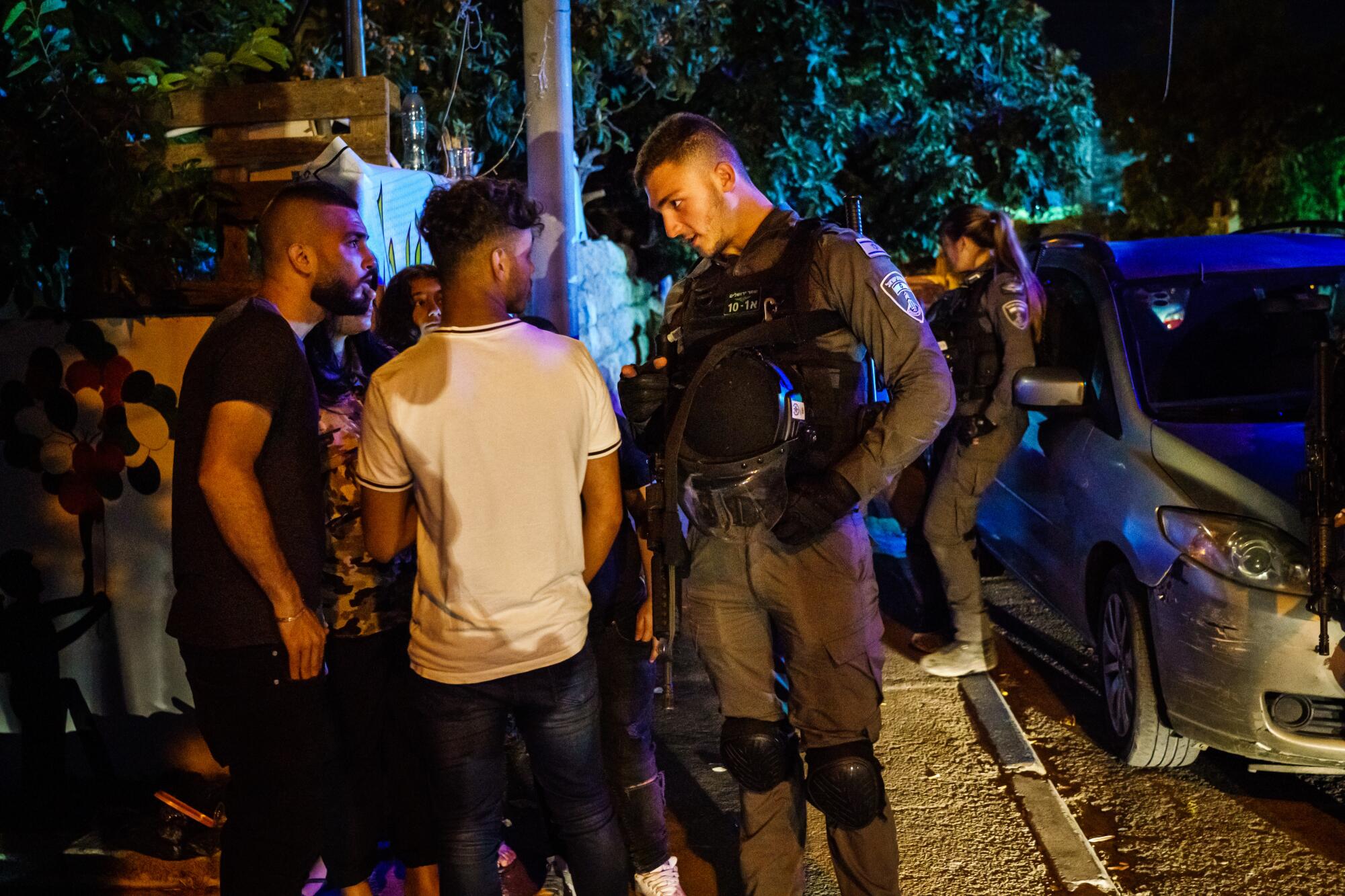 An Israeli security officer questions young residents on the streets of the Sheikh Jarrah neighborhood in East Jerusalem