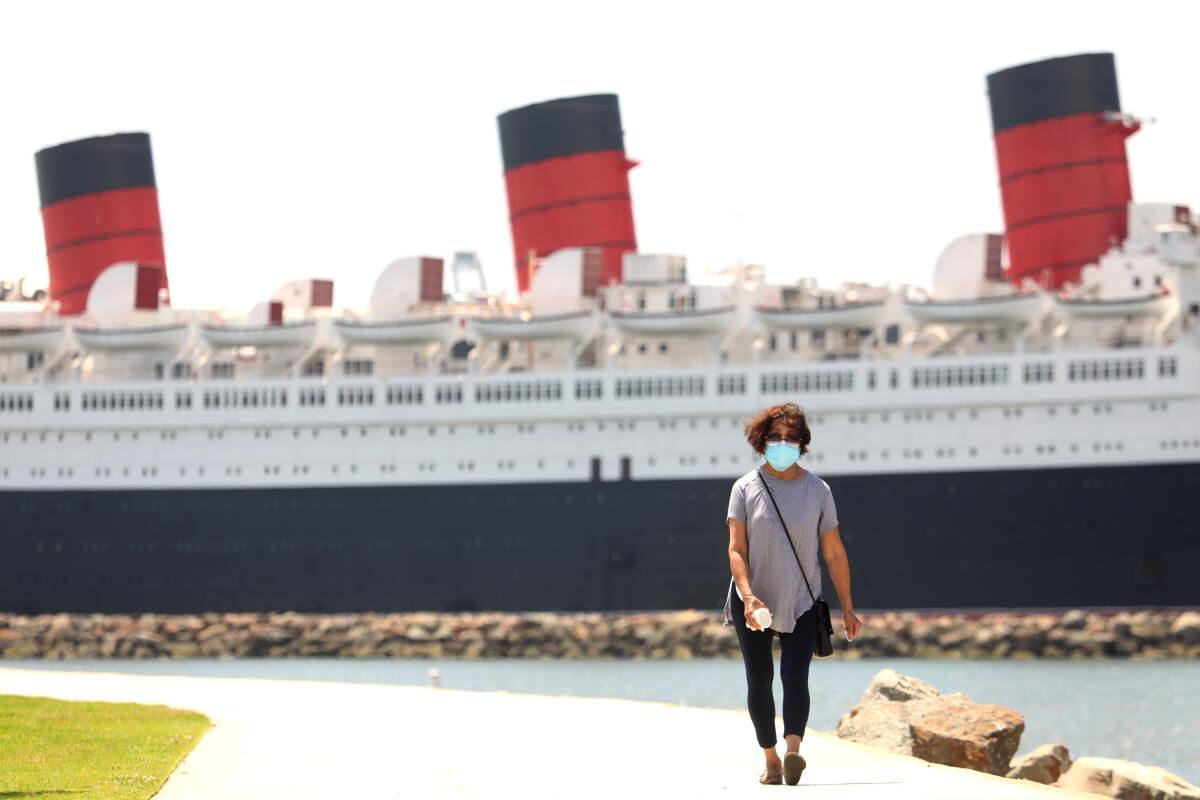 The Queen Mary, seen behind a woman walking on a bike and pedestrian path, has been docked in Long Beach since 1967.