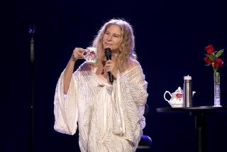 A woman in a white gown holds a microphone and cup of tea