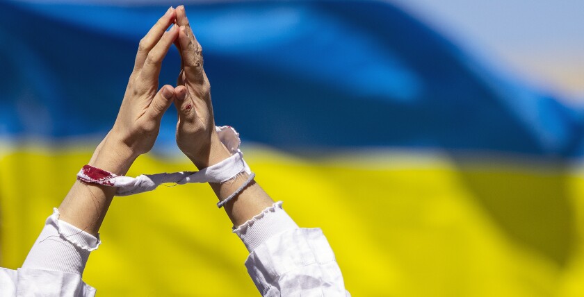 A demonstrator's hands, bound by mock bloodied handcuffs, are held high before a Ukrainian flag