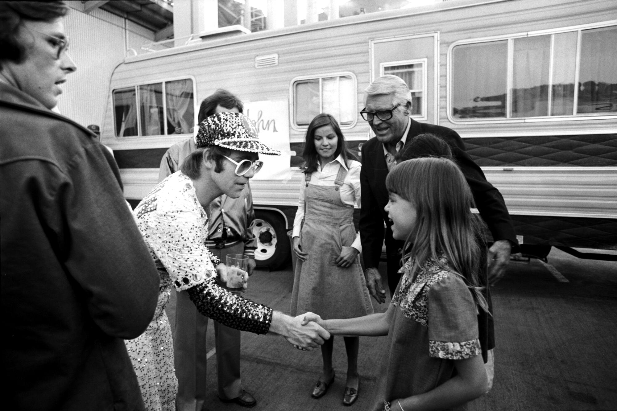 A musician in a sequined costume shakes hand with a young girl backstage