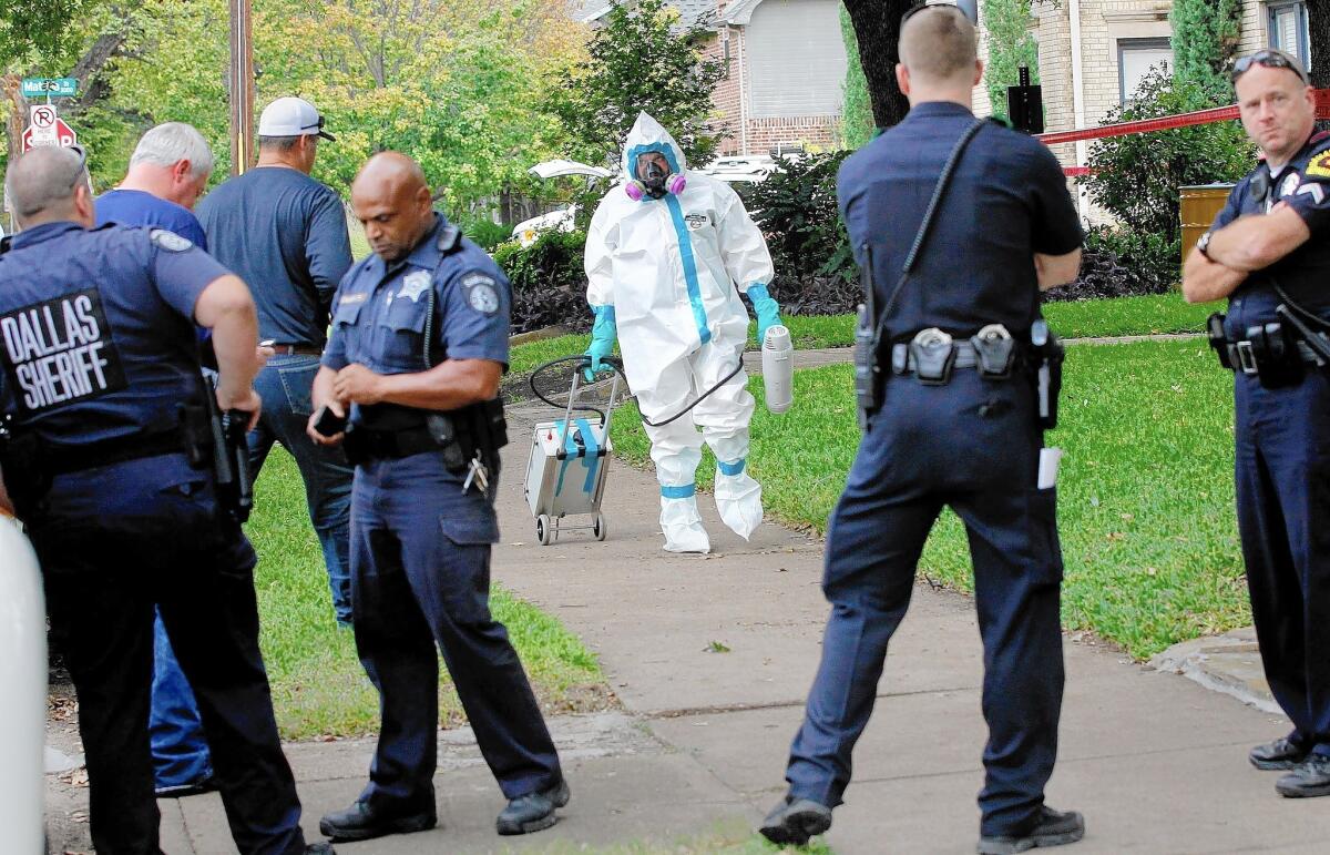 A man dressed in protective clothing leaves after treating the front porch and sidewalk of a Dallas apartment on Sunday where a second person diagnosed with the Ebola virus resides.
