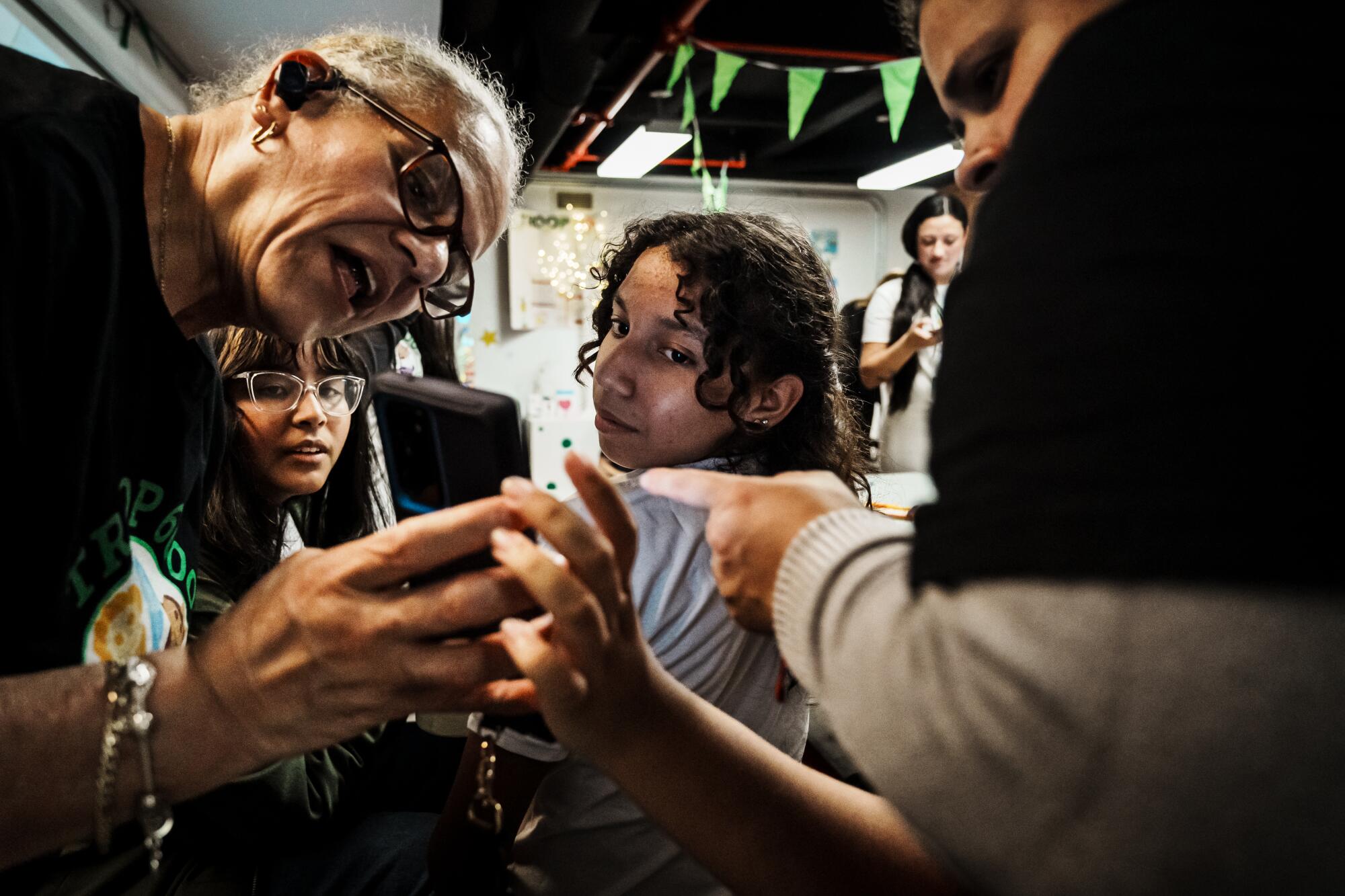 A woman holds a cell phone while the girls look at the screen.