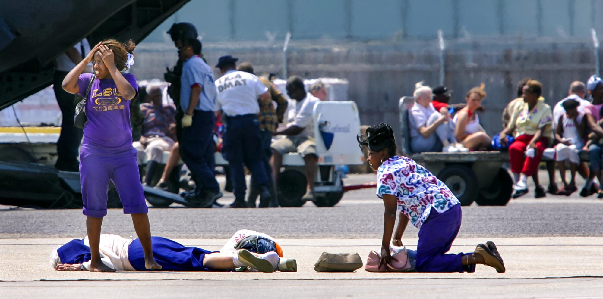 A woman looks around while another kneels by someone who's fallen