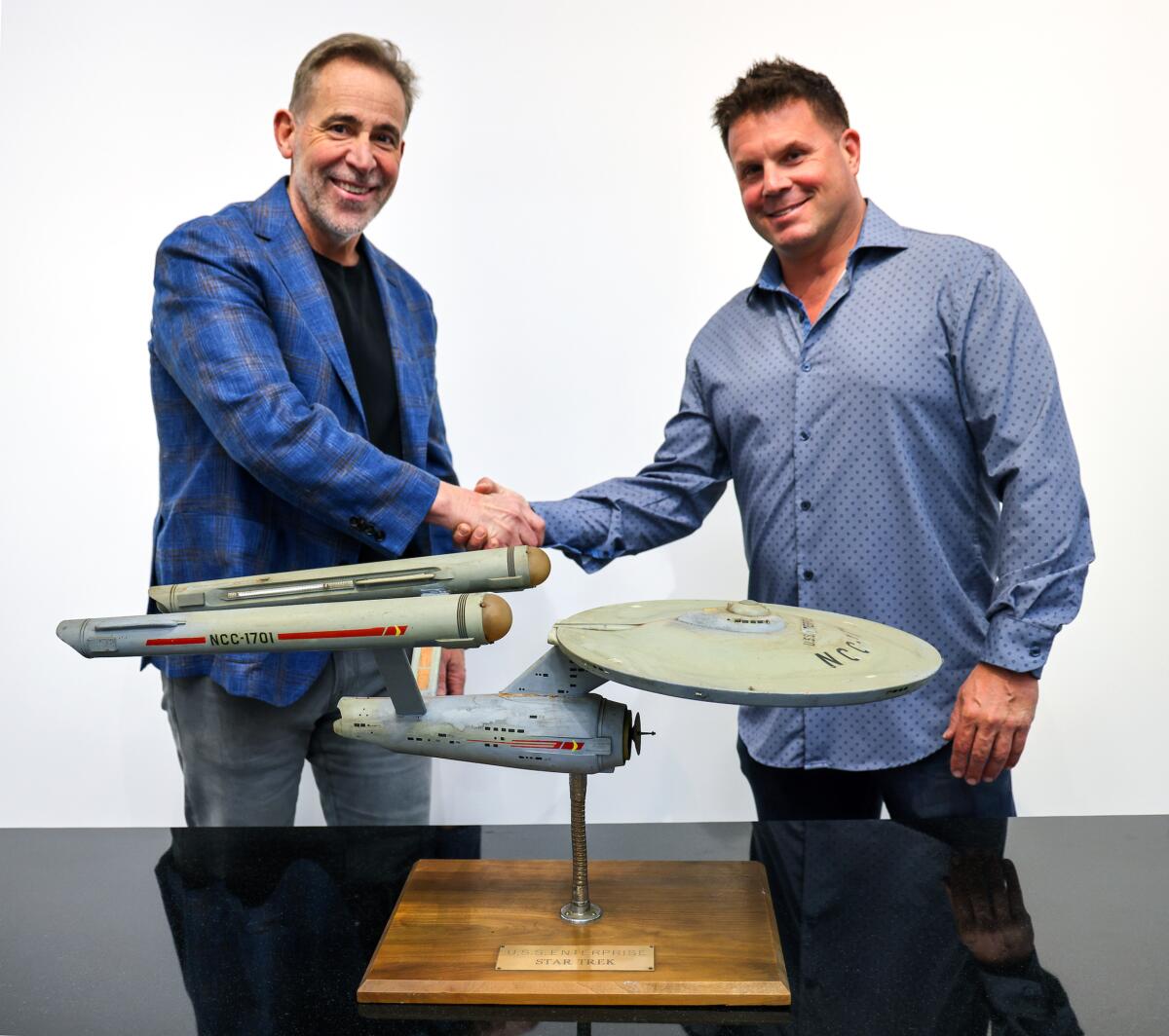 Two men shake hands next to a model of the U.S.S. Enterprise
