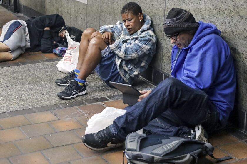 Los Angeles, CA - March 15: John Hargrave, PATH outreach worker, right, talks to a homeless woman Tracy Hellams, center, resting at the entrance of 7th. Street Metro station on Tuesday, March 15, 2022 in Los Angeles, CA. (Irfan Khan / Los Angeles Times)