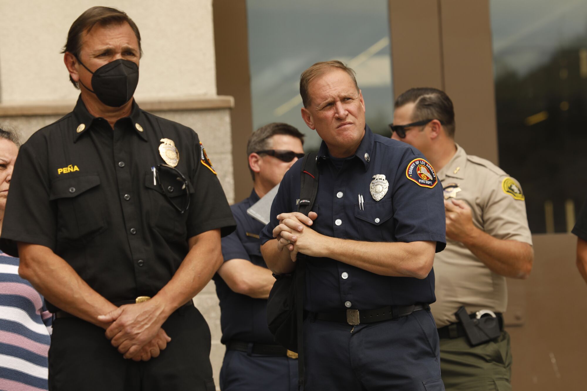 Two uniformed firefighters, one wearing a face mask, stare intently.