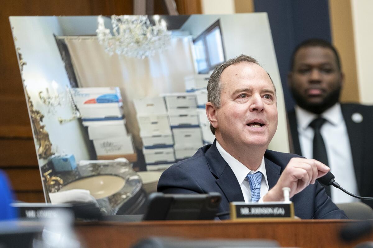 Rep. Adam Schiff speaks in front of a blown-up photograph of boxes stacked in a bathroom.