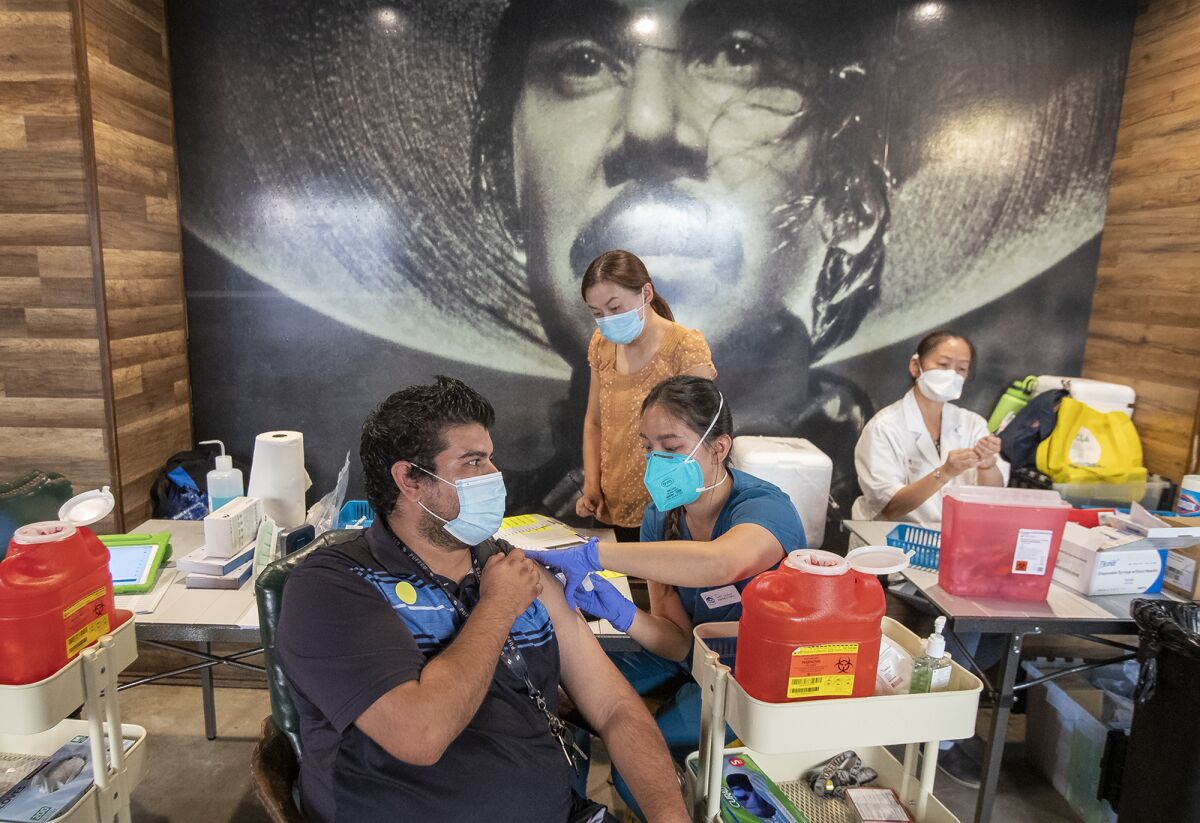 Gabi Caohui gives Johnnie Cruz a COVID-19 vaccination  at El Indio Botanas y Cerveza in Santa Ana.