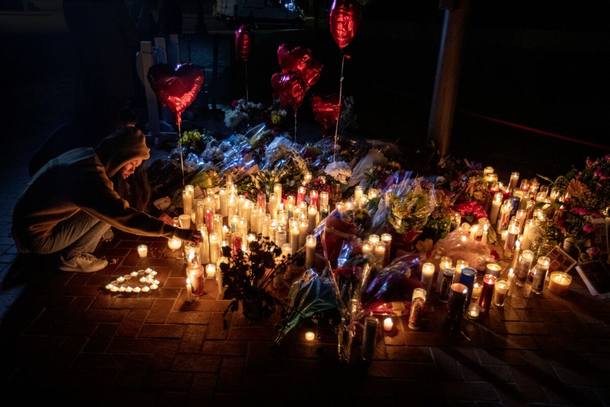 A person lights a candle at a nighttime memorial with candles, balloons and flowers