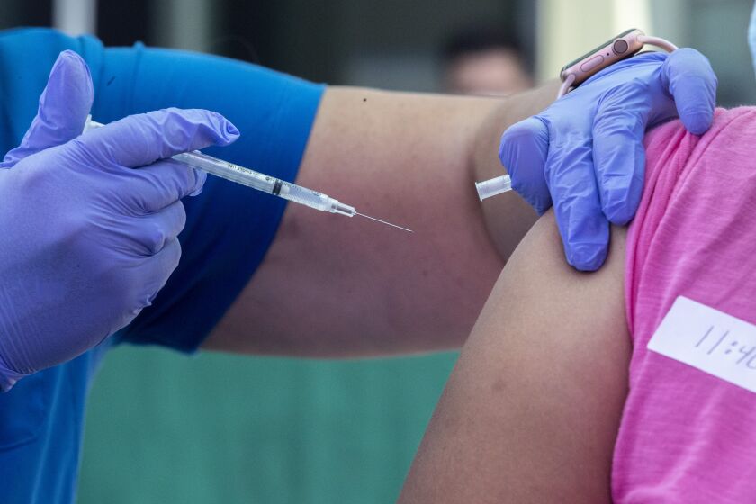 LOS ANGELES, CA - AUGUST 17, 2021- RN Amy Berecz-Ortega, left, inoculates a woman at a COVID-19 vaccine event hosted by councilman Curren Price on Tuesday, Aug. 17, 2021 in Los Angeles, CA. The first 200 people between the ages of 12 and 20 who got vaccinated at the event received a free pair of Beats by Dre headset. (Brian van der Brug / Los Angeles Times)
