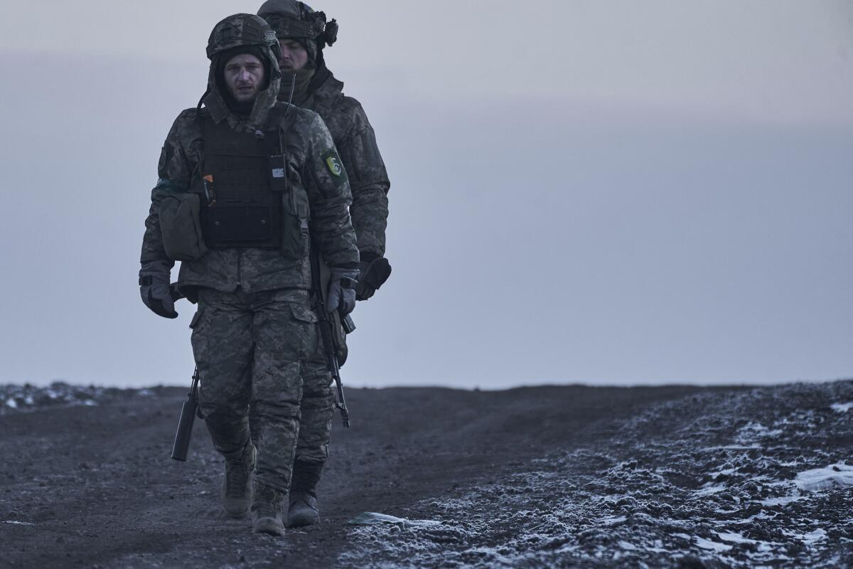 Two Ukrainian soldiers walk down a dirt path.