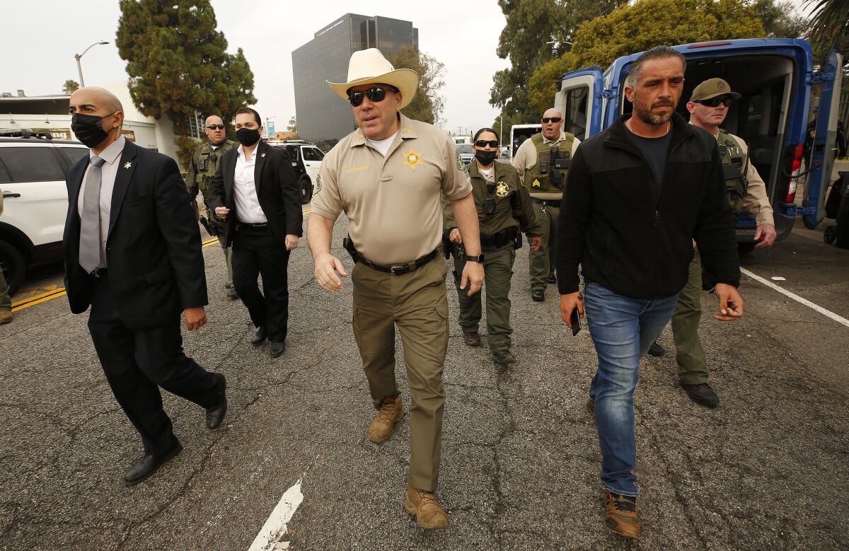 Sheriff Alex Villanueva walks down a street flanked by several other people.