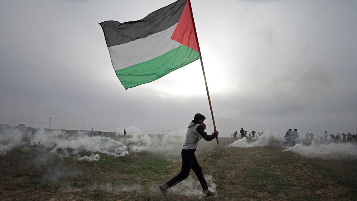 A protester carrying a Palestinian flag takes cover during clashes near the border with Israel east of Gaza City on Dec. 22, 2017.