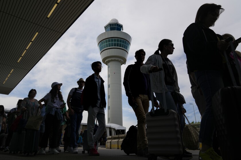 Travelers wait in long lines outside the terminal building to check in and board flights at Amsterdam's Schiphol Airport, Netherlands, Tuesday, June 21, 2022. The airport is reining in flight departures over its busy summer period because shortages of security staff mean it cannot cope with the high demand as many families take to the skies for the first time since the coronavirus pandemic has eased. The decision is likely to affect the vacation plans of thousands of travelers each day, the airport's CEO said.(AP Photo/Peter Dejong)
