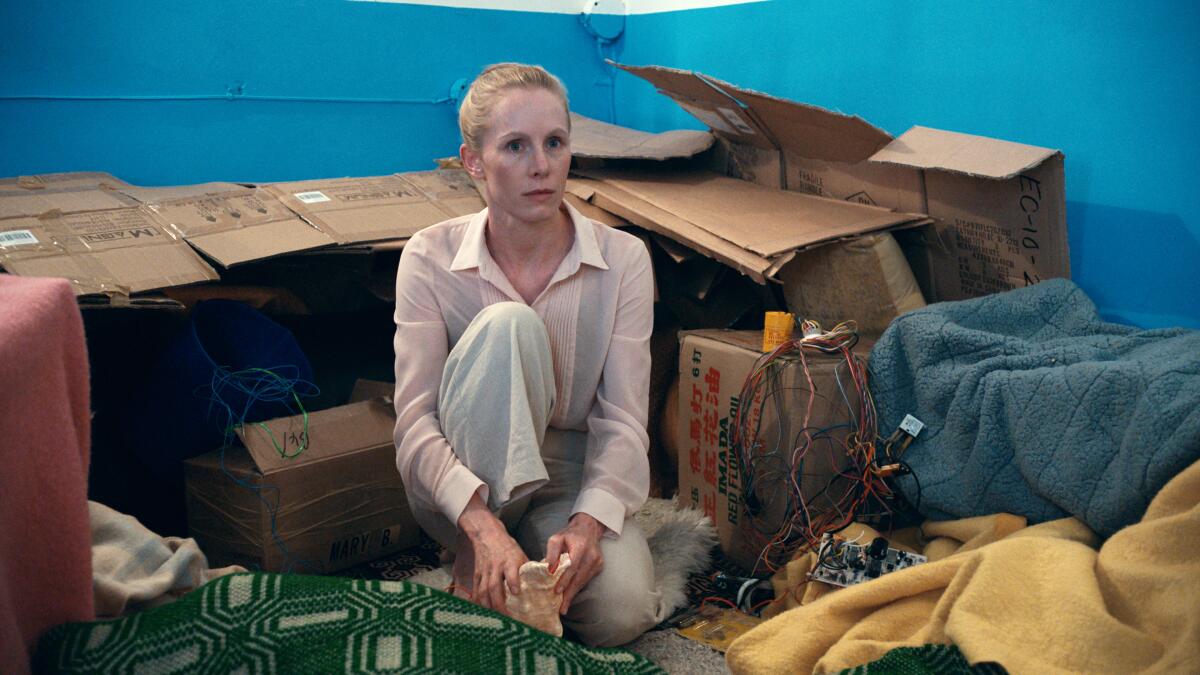A woman sitting on the floor amid boxes and blankets.
