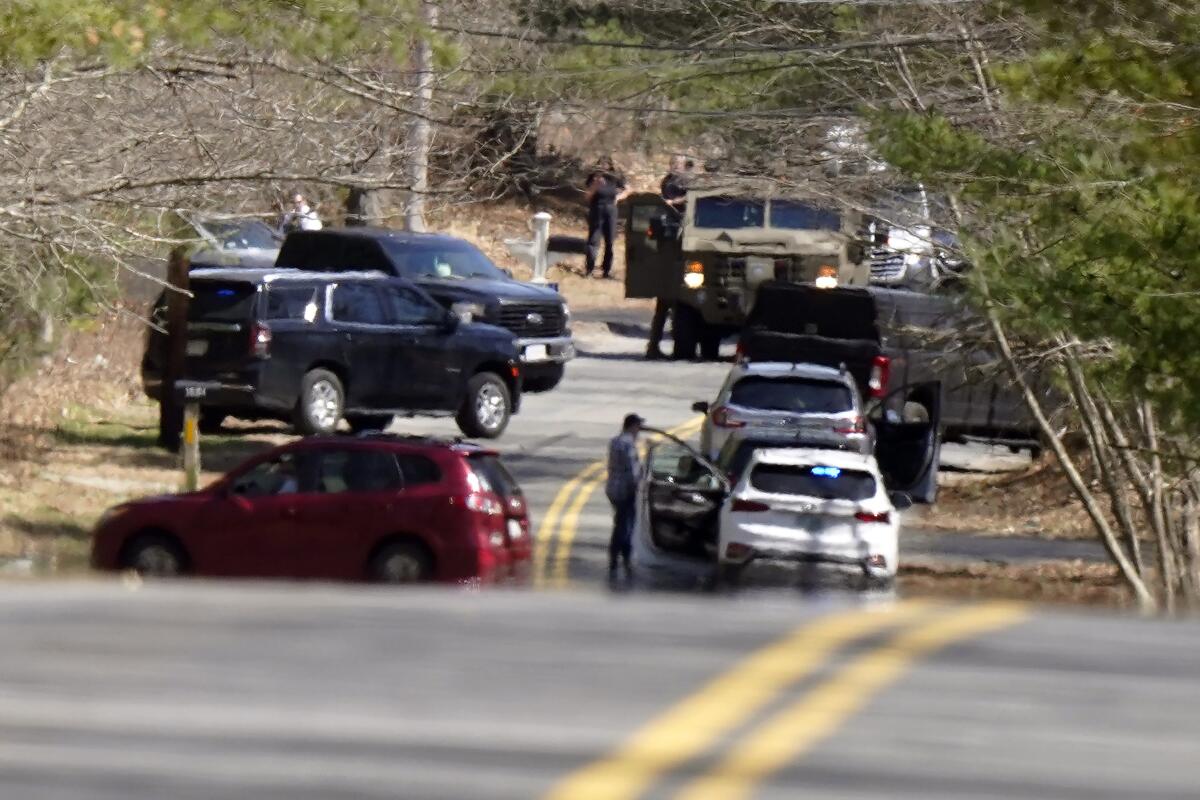 Law enforcement and military vehicles block a tree-lined two-lane road