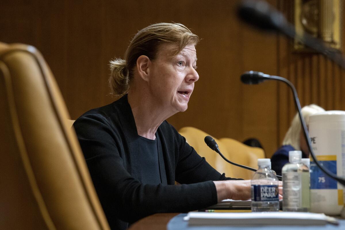 Sen. Tammy Baldwin speaking into a microphone while seated on the dais at a hearing