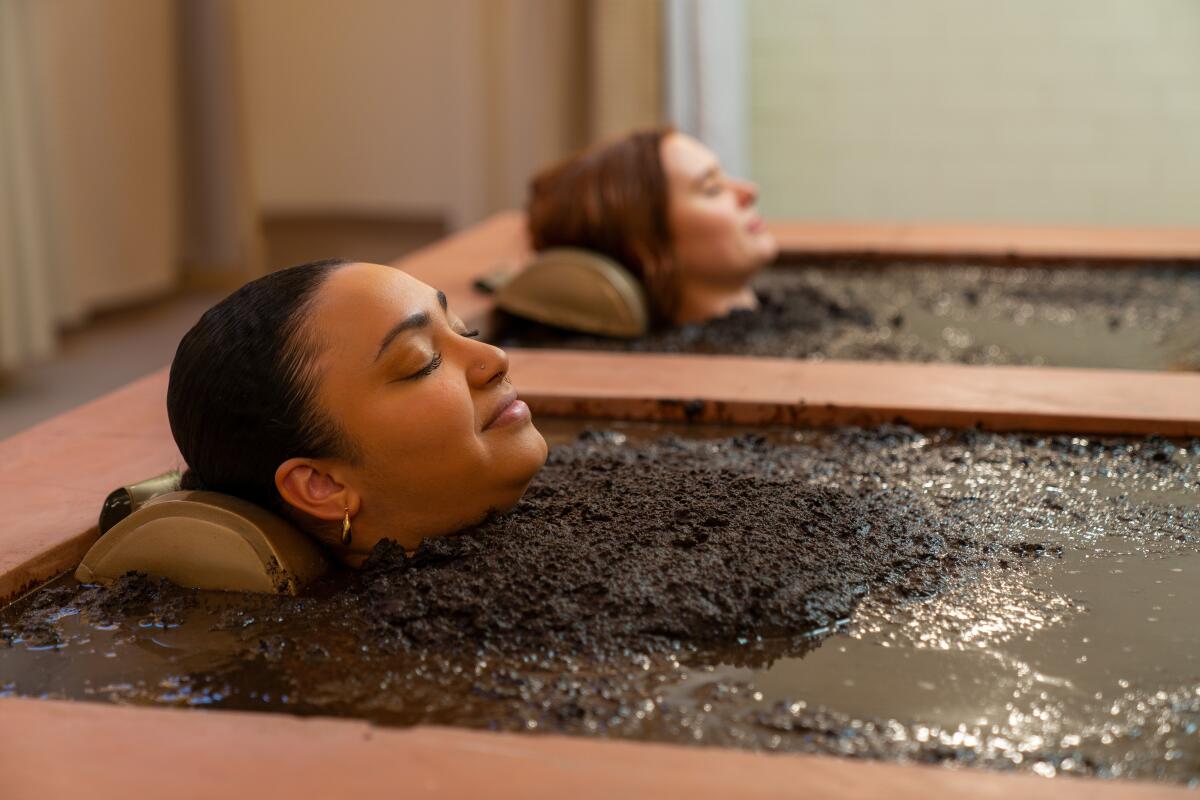 Two women with only their heads sticking out of their mud baths