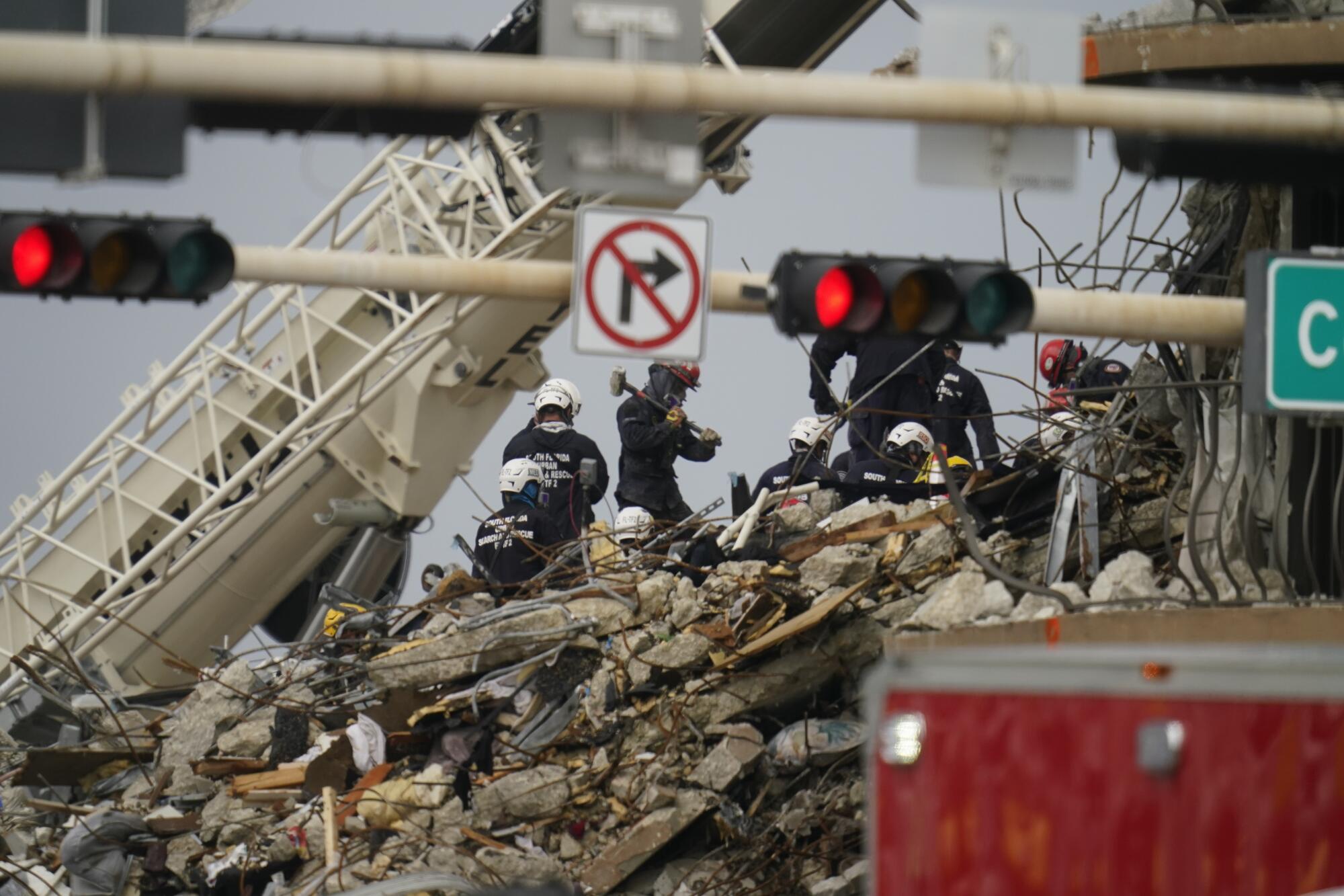 Rescuers in helmets stand atop rubble near a crane.