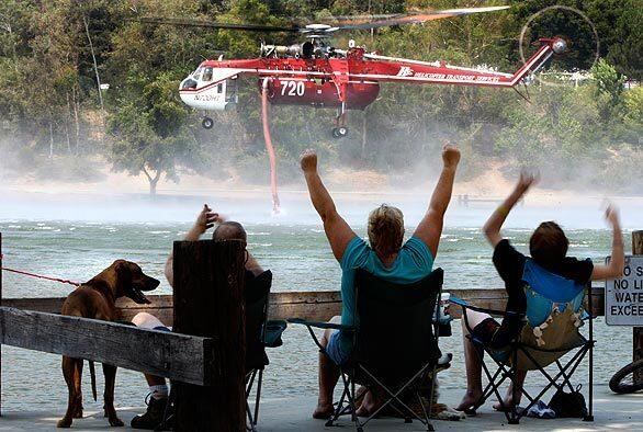 From a lakeside dock in Yucaipa Regional Park, the McHenry family cheers as a Sikorsky S64 Sky Crane firefighting helicopter goes "In the Dip" for another load of water Tuesday. The parents and their son spent the night camping in the park after receiving a mandatory evacuation order from their nearby home. By about midday, half dozen aircraft were dousing hot spots in the all but extinguished Pendleton and Oak Glen fires. Cal Fire officials kept all firefighters and gear in the park in case lighting strikes or wind start new fires overnight.