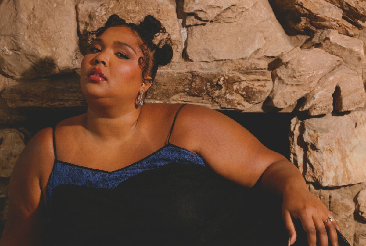 A woman with two hair buns poses for pictures in a blue thin-strapped dress.