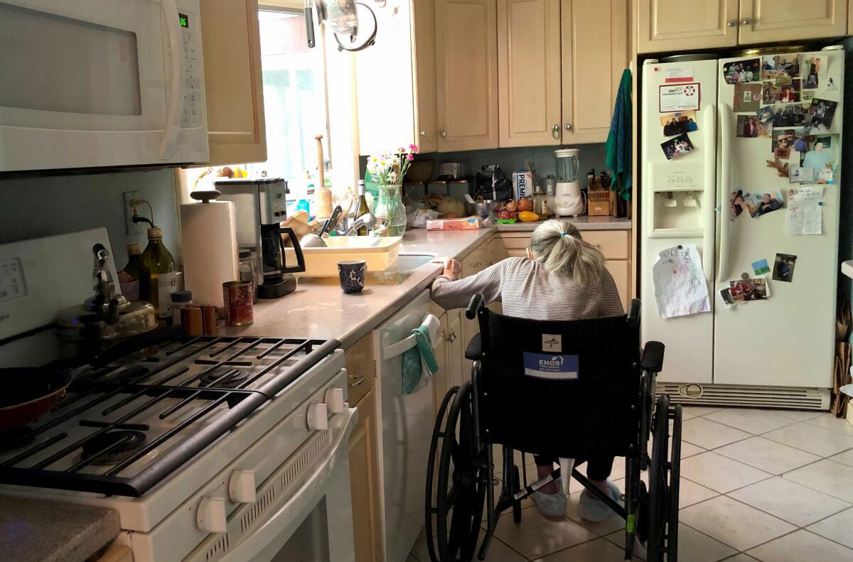 A woman sits with her back to the camera in a wheelchair in her kitchen