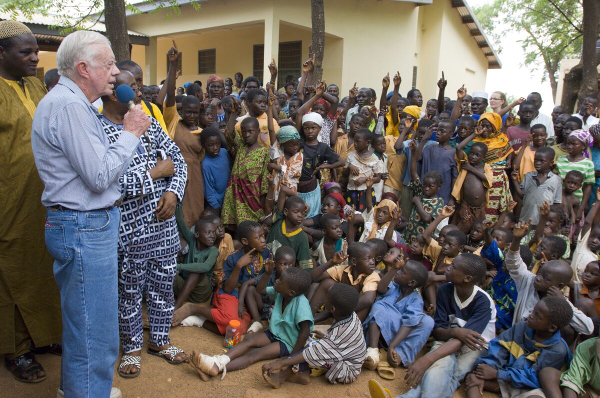 Jimmy Carter speaks into a microphone as a group of youths and adults look on