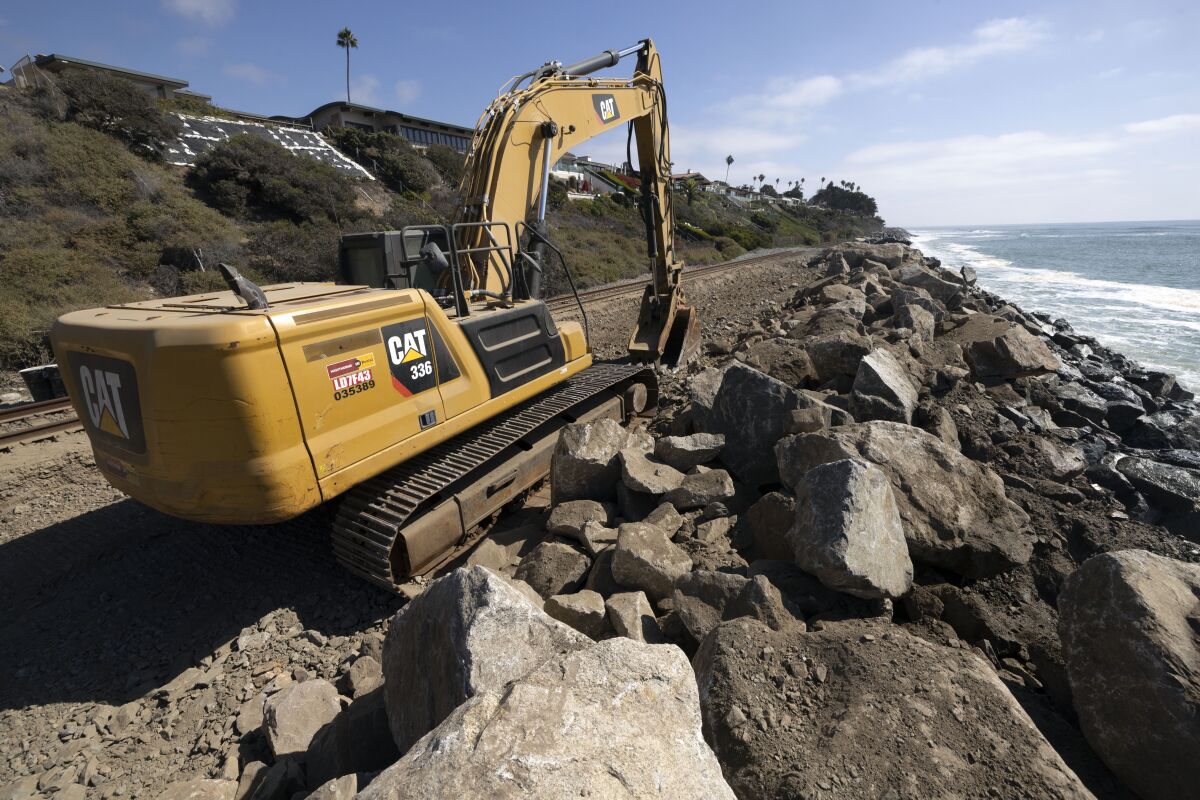 An excavator next to railroad tracks running along the ocean