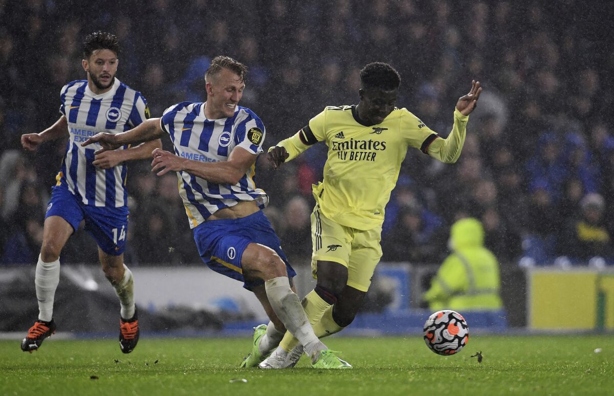Brighton and Hove Albion's Dan Burn and Arsenal's Bukayo Saka, right, battle for the ball during the English Premier League soccer match at the AMEX Stadium, Brighton, England, Saturday Oct. 2, 2021. (Ashley Western/PA via AP)