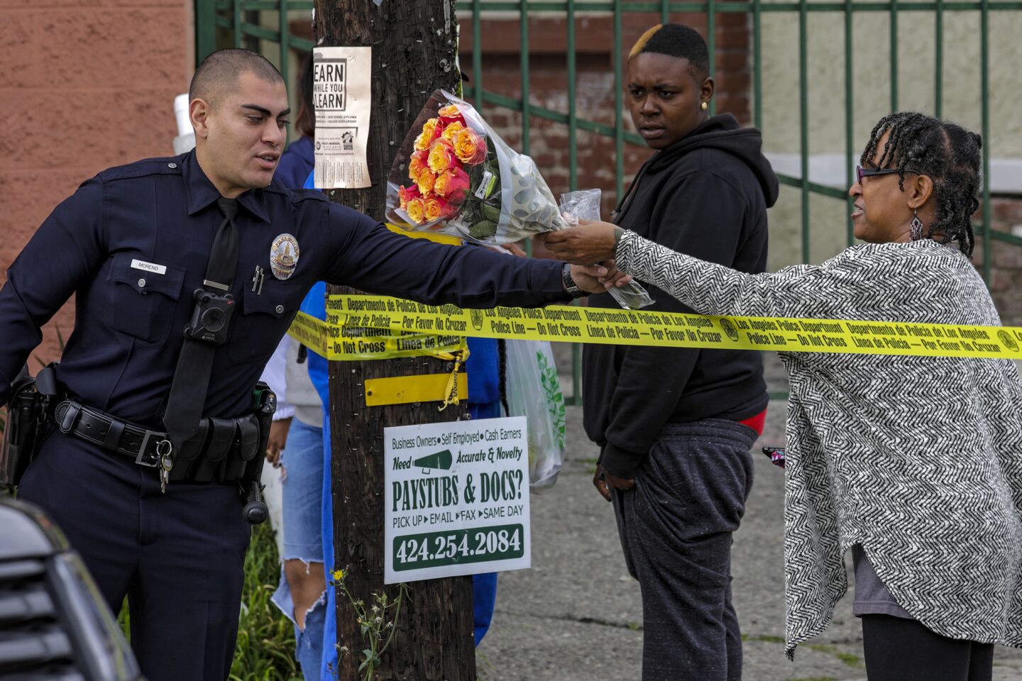 LAPD officer Jonathan Moreno, left, receives a bouquet from Rochelle Trent, 64, to be placed at a makeshift memorial for Nipsey Hussle on April 2.