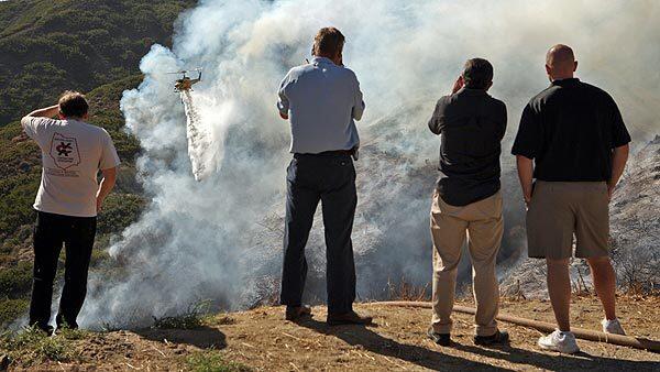 Residents of the Camarillo Heights neighborhood watch as Ventura County helicopters drop water on smoldering brush Tuesday afternooon. Four helicopters made water drops as hand crews worked to cut brush lines. See full story