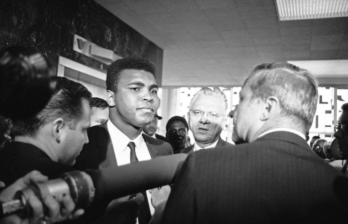 Muhammad Ali, center, and his attorney Hayden Covington, right, wait for the elevator to take them up to the federal court in Houston, Texas, where Ali was being charged with refusing to be inducted into the armed services.