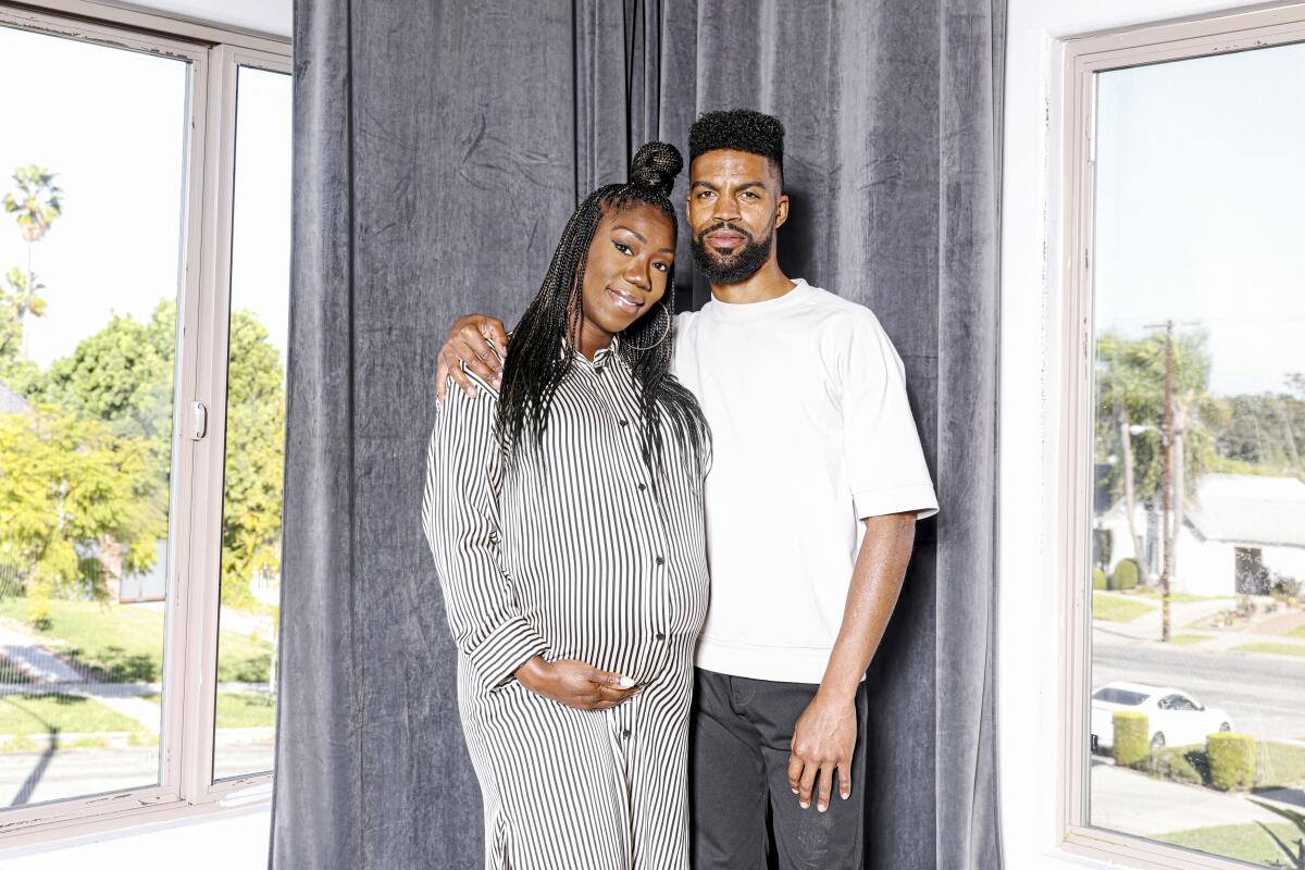 A pregnant woman smiles at the camera next to a man standing with his arm around