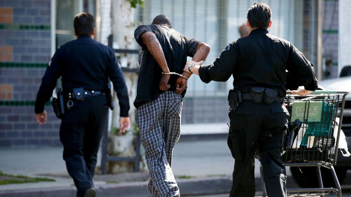 LAPD officers arrest a man on skid row in 2016 for possession of a stolen shopping cart during a sweep with sanitation crews.