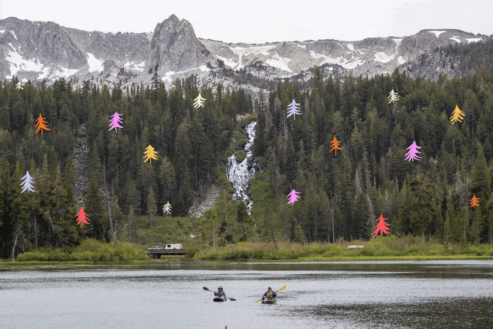 Two kayaks on a lake are seen from a distance, backed by mountains and evergreens.