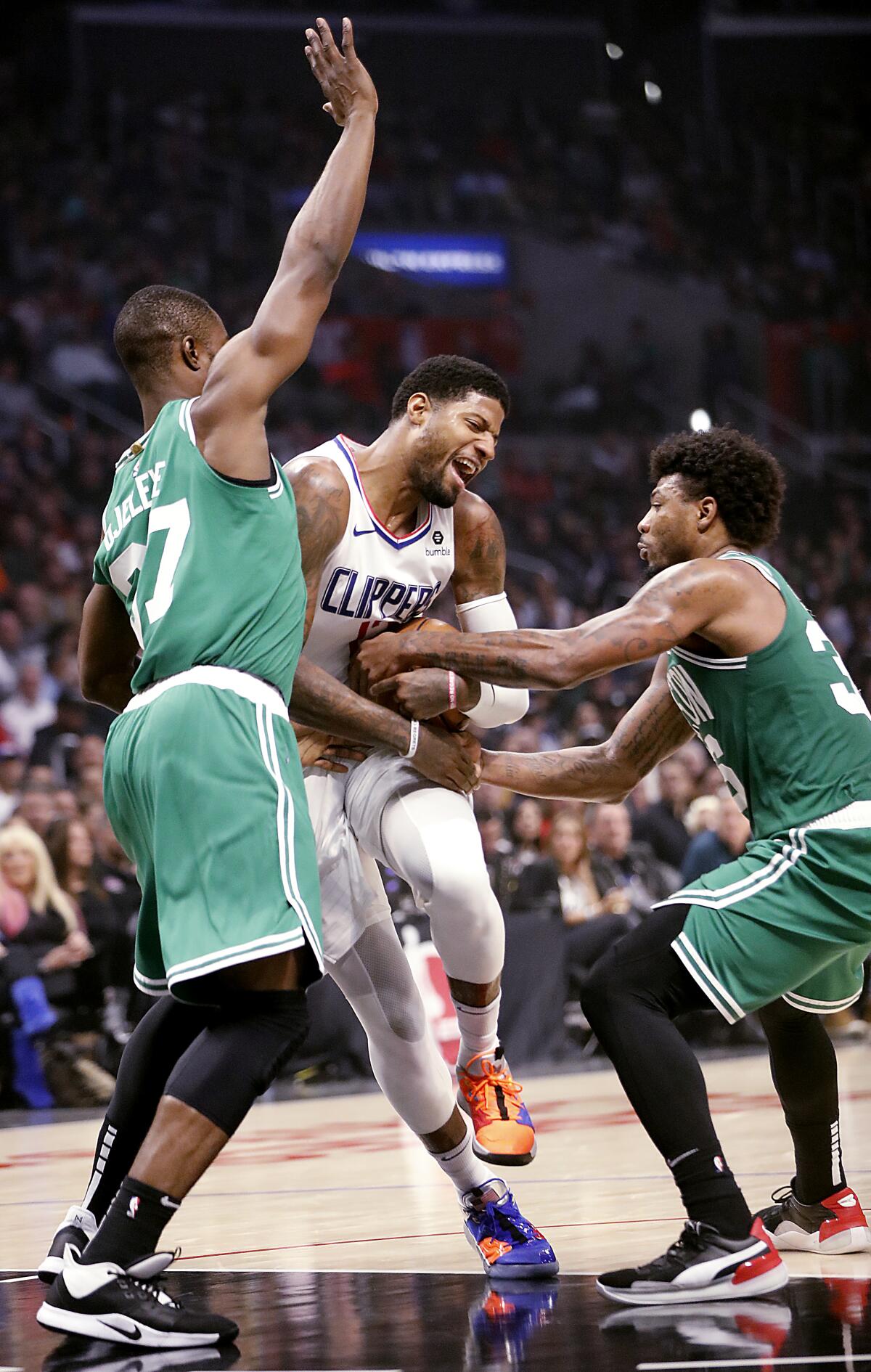 Clippers forward Paul George, center, gets fouled on a drive between Boston defenders Semi Ojeleye and Marcus Smart during the second quarter of their game Nov. 20, 2019, at Staples Center.