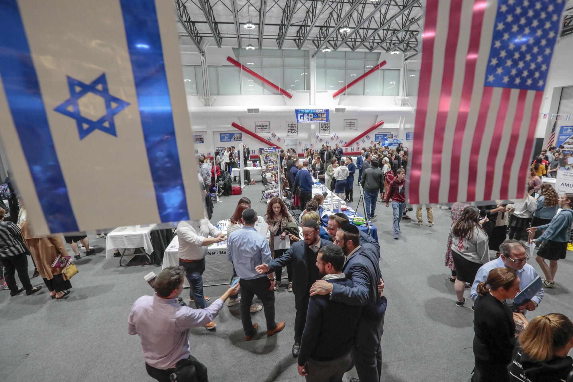 People fill a large room where large flags of Israel and the United States hang from the rafters.