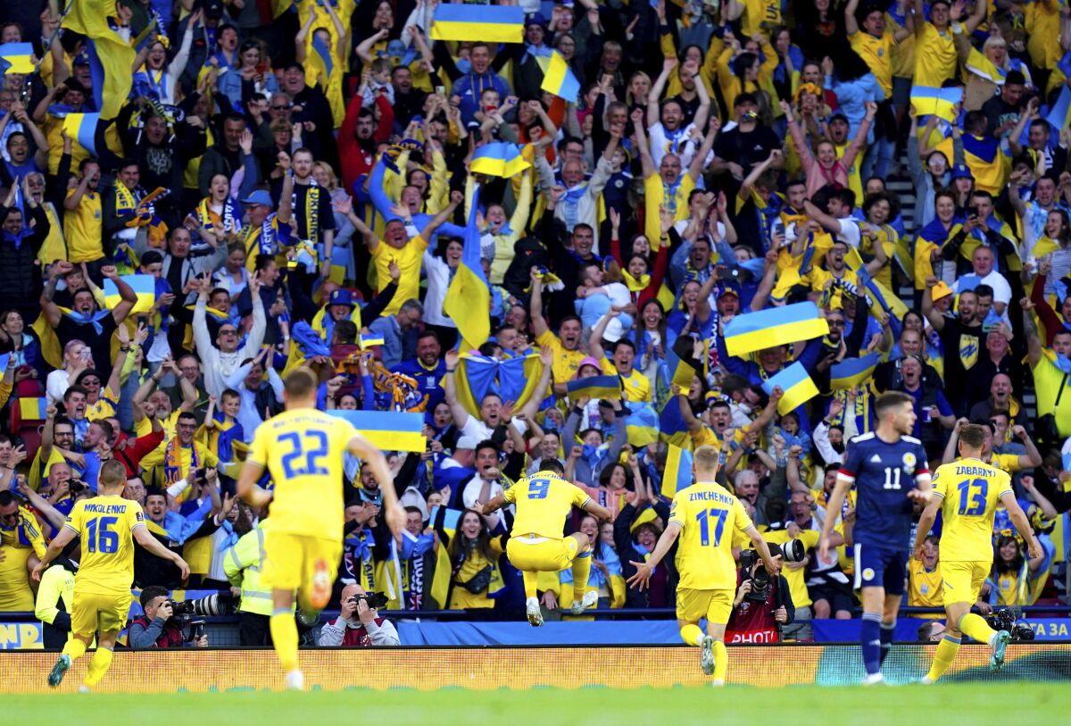 Soccer players wearing yellow run toward fans with raised arms, some holding blue-and-yellow flags, in a stadium