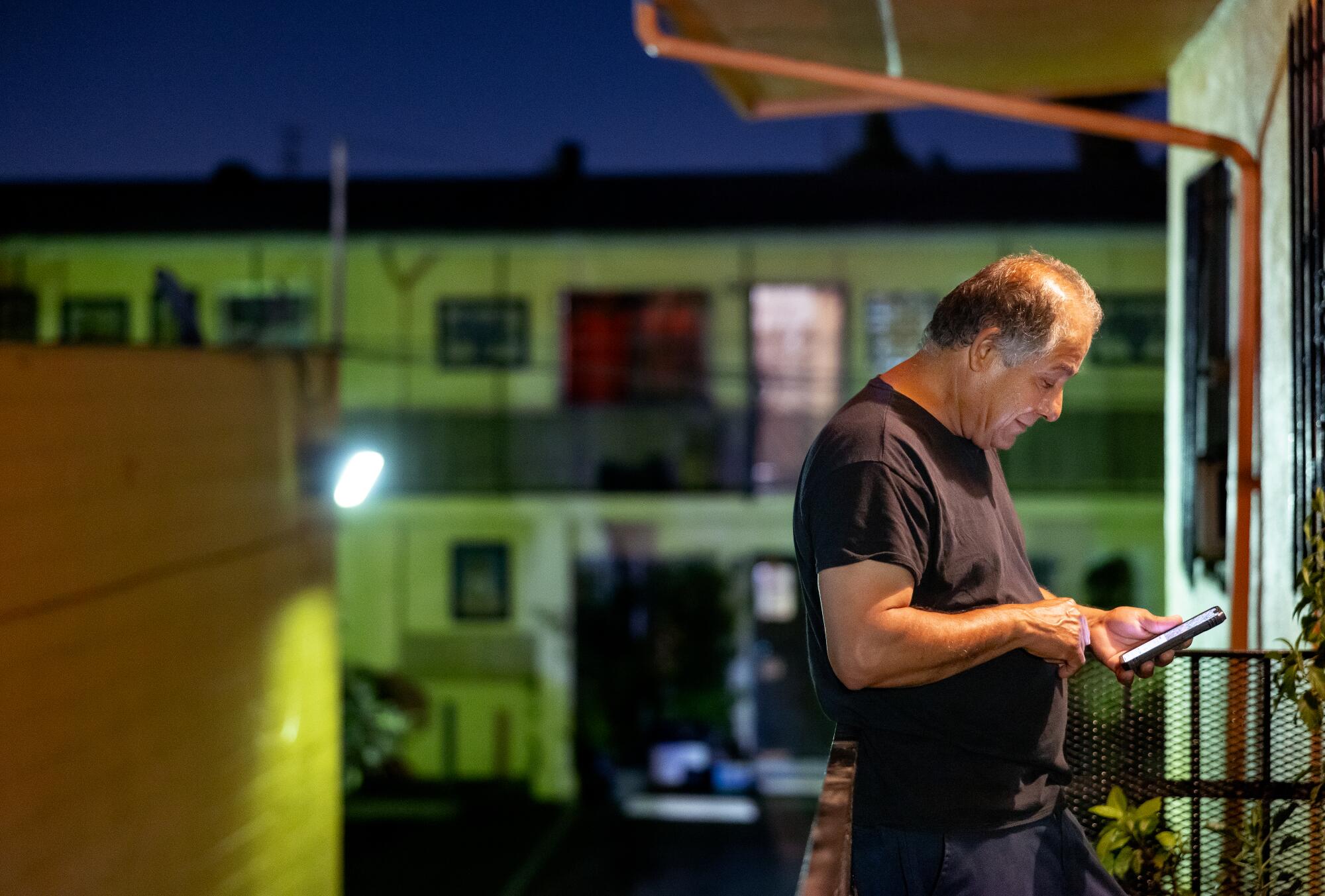a man looks at his cellphone while standing out on a balcony at night