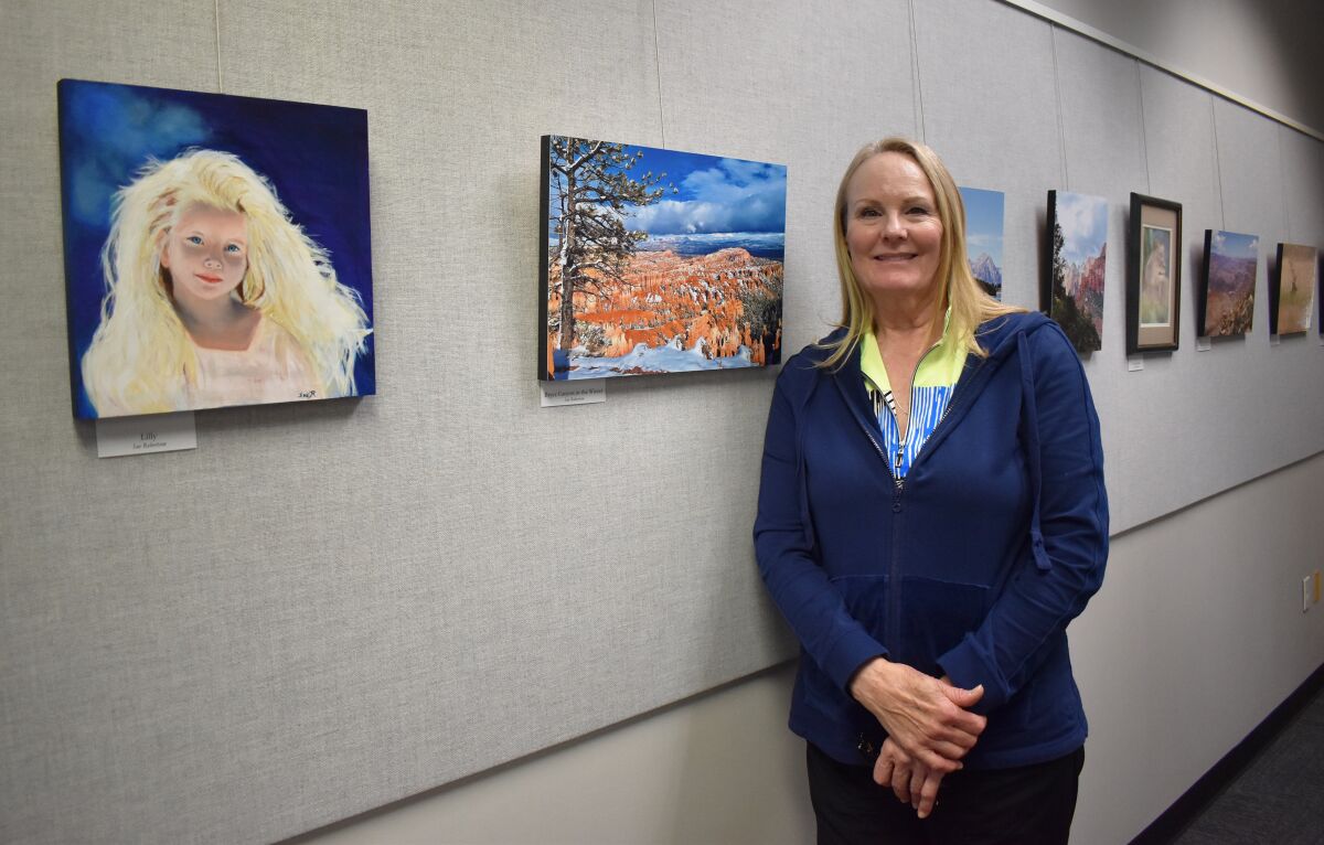 Artist Sue Robertson standing near her paintings and photographs displayed in the Rancho Bernardo Library.