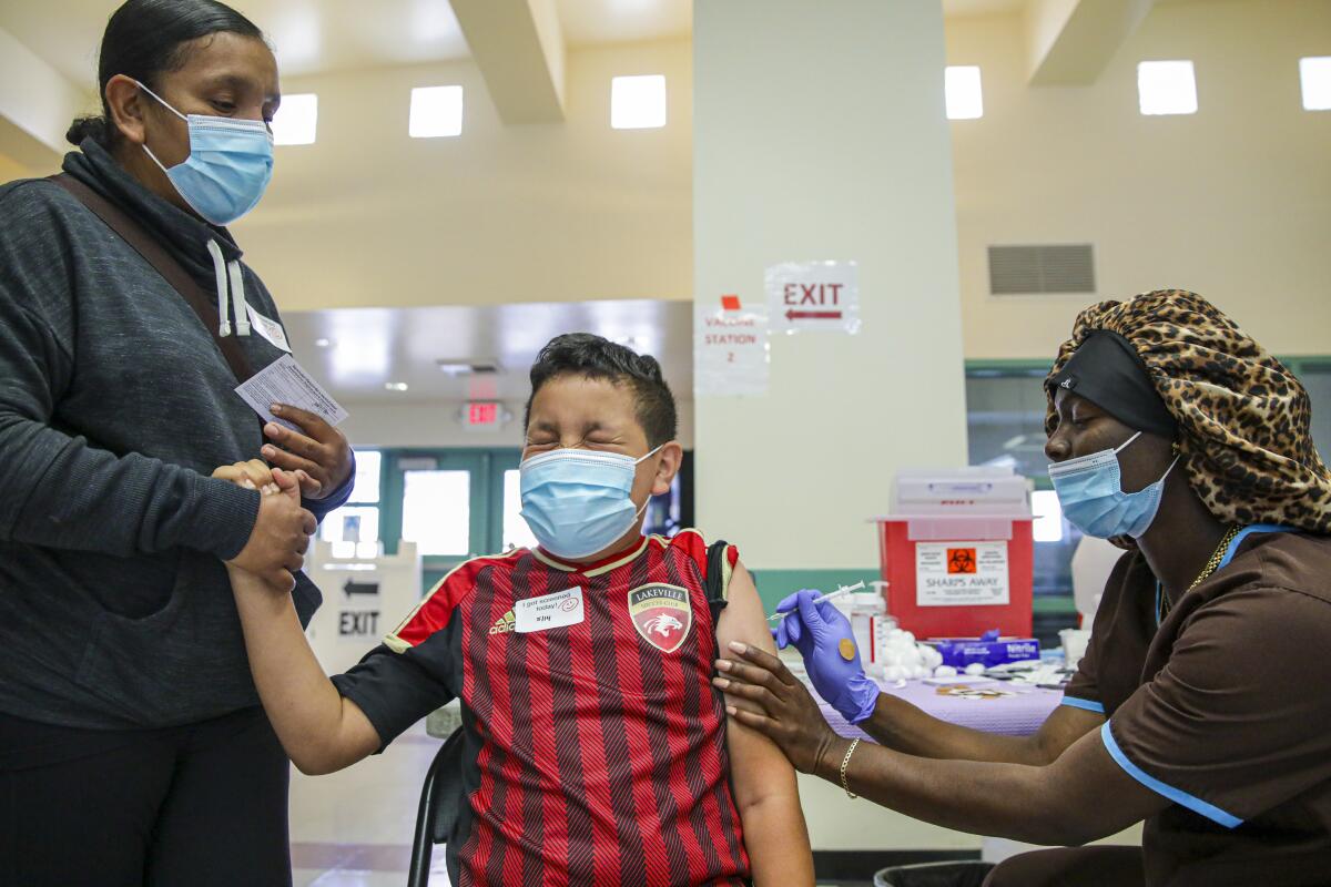 A boy holds his mother's hand as he receives a vaccination